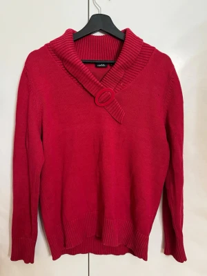 Röd stickad tröja från Isolde - Mysig och unik stickad tröja i en härlig hallonröd nyans från Isolde. Tröjan har en fantastisk krage med ribbade detaljer och en dekorativ, matchande ring framtill som ger plagget en retro-modern känsla. Ribbstickade muddar nertill och vid ärmsluten ger en fin passform. En perfekt färgklick i garderoben som livar upp vilken outfit som helst! • Märke: Isolde • Storlek: L • Färg: Hallonröd / Röd • Skick: Mycket fint skick