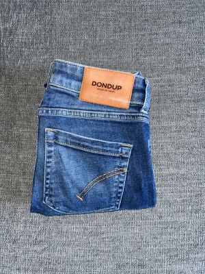 Blå Dondup jeans - Snygga blå jeans från Dondup med klassisk femficksdesign och brun läderpatch bak. Jeansen är skinny modell, strl: midja  37cm insida ben 69,5cm.  Perfekta för dig som gillar stilrena och tidlösa jeans. Priset är prutbart. Hör av er vid intresse/ frågor!