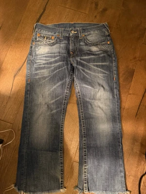 True Religion bootcut jeans blå - Säljer ett par blå bootcut jeans från True Religion med slitna, fransiga benslut och klassiska kontrastsömmar. Jeansen har fem fickor och en ikonisk patch bak i midjan. Säljer för att stilen som jag haft fallit ur och vill hellre ha lite mer regular fit trueys. Dock så är dessa ganska så använda, som man ser längst ner. Skriv vid frågor😇😇