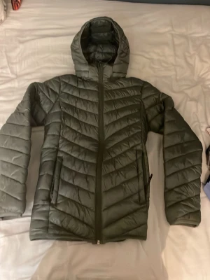 Mörkgrön pufferjacka med huva - Säljer en mörkgrön pufferjacka från mckinley .Jackan har huva, hel dragkedja framtill och snygga quiltade detaljer i ett pilformat mönster. Tillverkad i syntetmaterial och passar perfekt för kyligare dagar.