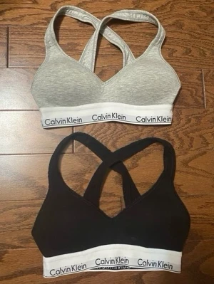 Calvin Klein bh - Två push up bh linnetoppar från Calvin Klein (NY PRIS 500kr st) En är svart i storlek M och en är ljusgrå i storlek S. De har korsade axelband i ryggen och är tillverkade i mjuk bomullsblandning. Perfekta för en chill look eller träning.