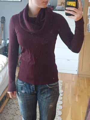 Vinröd polotröja från Soya Concept - Vinröd polotröja från Soya Concept med bred, ribbad polokrage och långa ärmar. Tröjan har ribbade muddar vid ärmslut och nederkant, och är i en mjuk, stretchig stickad kvalitet. 