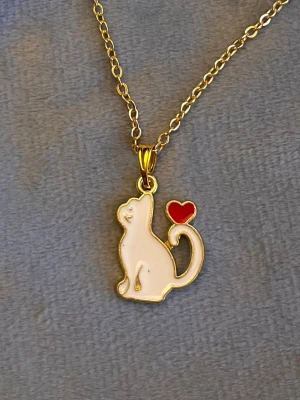 Halsband katt med hjärta guld imitation   - Sött halsband med en berlock i form av en katt med ett hjärta. Berlocken är ca 2 x 0,5 cm. Trädd på kedja i guldimitation som är justerbar 40-45 cm. 