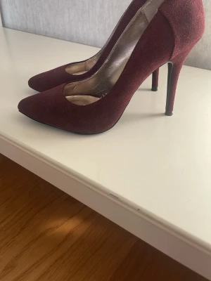 Vinröda mockapumps från Steve Madden - Snygga vinröda pumps från Steve Madden i mjuk mocka. Skorna har spetsig tå och hög klack som ger en elegant siluett. Insidan är metallicfärgad och de har en klassisk, stilren look som passar till många outfits.