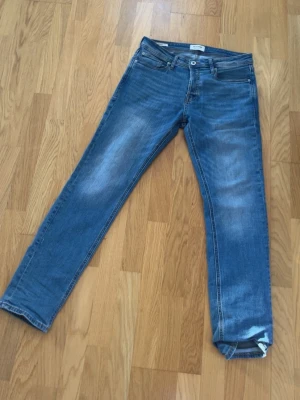Blå raka jeans från Jack Jones - Säljer ett par klassiska blå jeans från Jack Jones  Jeans med raka ben och normal passform. Jeansen har fem fickor, ljus tvätt och subtila slitningar framtill för en avslappnad look. Tillverkade i bomull med Jack Jones  på bakfickan.