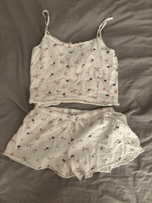 Vit blommig pyjamas från lager 157🫶🏻 - Säljer ett gulligt pyjamasset från 157 i storlek S. Setet består av ett linne med tunna axelband och matchande shorts, båda i vit bomull med små blommiga mönster i rosa och blått. Shortsen har en söt knytning i midjan. Perfekt för mysiga kvällar!🤍