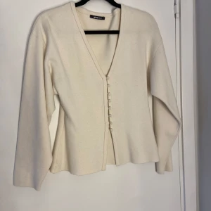 Vit kofta med knappar från Gina Tricot - Snygg vit kofta från Gina Tricot i storlek M. Koftan har v-ringning och dekorativa tygklädda knappar framtill. Materialet är mjukt och stickat, med långärmade ärmar och en loose passform. Sparsamt använd