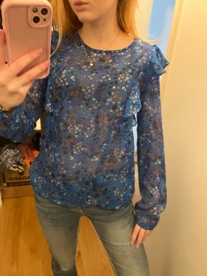 Blå genomskinlig blus med blommigt mönster  - Blå tröja med volang på axlarna 