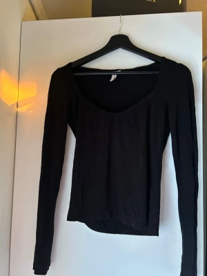 Svart långärmad topp från Nelly - Nelly – svart långärmad topp med djup ringning (basic) Figurnära, stretchig jersey. Klassisk basmodell. Har även en likadan i vinröd!  Super vacker, enkelt men klassisk söm av spets vid ringningen. HAR ÄVEN EN LIKADAN MODELL I VINRÖD FÄRG. 