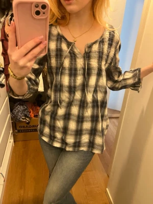 Rutig blus från N.Y. NearYou - Säljer en luftig rutig blus från N.Y. NearYou i storlek 38. Blusen har blå, grå och vita toner, trekvartsärm och knytning vid halsen. Känns som S