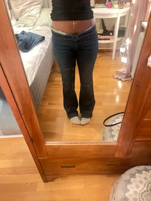  jeans med slitningar - Säljer ett par mörkblå jeans med bootcut passform och slitna detaljer vid knäna. Det har en lagning vid innerlår som inte syns när man har på sig de. De är köpt second hand så vet inte va de är för märke.