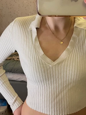 Vit ribbad croppad polotopp  - Säljer en vit  ribbat material och v-ringning. Toppen har långa ärmar och en krage. Säljer en vit ribbad tröja som har en passform med kortare mage. Tröjan har v-ringning och en krage. Den är lite smutsig/grå vid ärmarna men det är inget man tänker på så mycket. Går att använda både med och utan linne under. Materialet är 45% viskos, 40% akryl och 15% polyamid. Skriv för fler bilder om mått för de fick inte plats.