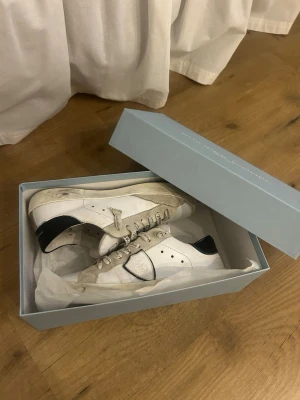 Philippe Model vita sneakers med svart häl - Säljer ett par snygga Philippe Model sneakers i vitt med svart häl och beige detaljer. Skorna har rund tå, platt sula och coola snören med textprint. Tillverkade i skinn och mocka, med klassisk logga på sidan. Perfekta för dig som gillar stilrena och trendiga sneakers. Priset går att diskutera. Skriv för funderingar eller fler bilder 