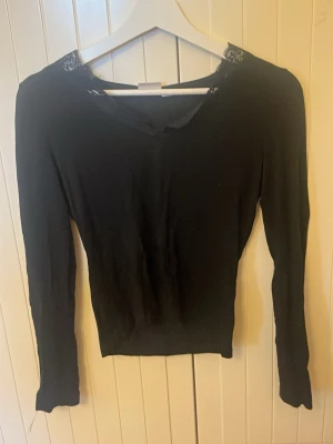 Svart långärmad topp med spets Gina Tricot - Svart långärmad topp från Gina Tricot med v-ringning och snygga spetsdetaljer runt halsen. Säljer billigt pga har klippt lite i v- ringningen för bättre passform