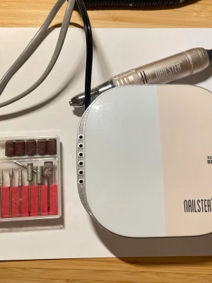 Elektrisk nagelfil från Nailster - Säljer en elektrisk nagelfil från Nailster med bits i olika former och sliprullar. Maskinen är vit och beige med metallicdetaljer och har tydlig RPM-markering. Perfekt för att fixa naglarna hemma med proffsigt resultat. Nypris 1300