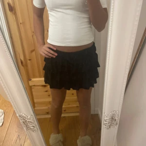 Svart volangkjol från Zara - Säljer en svart kort volangkjol från Zara. Kjolen har flera lager med volanger som ger en snygg och lekfull look. Den är tillverkad i mjukt bomullsmaterial och har en elastisk midja för skön passform. Perfekt för dig som gillar trendiga och bekväma plagg.