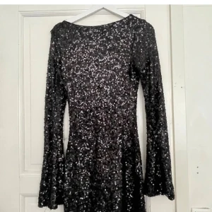 Svart glittrig paljettklänning Nelly - Glittrig svart kortklänning från Nelly med långa ärmar och figurnära passform. Hela klänningen är täckt av svarta paljetter som ger en riktigt festlig look. Perfekt för dig som vill sticka ut och glänsa hela kvällen. Trådar sticker ut men syns inte så mycket 