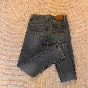 Nude Jeans ljusblå  - Säljer ett par ljusblå jeans från Nude Jeans med klassiska orangea sömmar och snygga detaljer på bakfickorna. Jeansen har ett ny pris på 1600kr men säljer endast för 349!
