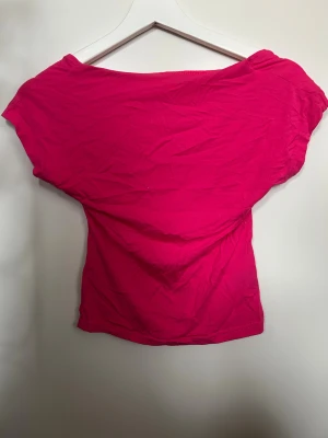 Rosa topp - Säljer en snygg rosa topp med offshoulder-design och öppen rygg. Modellen är tight och croppad, perfekt för dig som gillar att sticka ut. Materialet känns som mjuk bomull och färgen är riktigt poppig och ungdomlig.