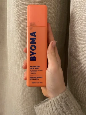 BYOMA Balancing Face Mist 100ml - Fräsch och färgglad orange face mist från BYOMA med blå text. Innehåller Tri-Ceramide Complex, probiotika och allantoin för att boosta hudbarriären. Praktisk, rektangulär plastflaska på 100 ml som är enkel att ta med i väskan.