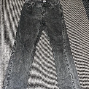 Grå straight jeans från Grunt - Säljer ett par grå jeans med tvättad och lite sliten look. Modellen är straight med klassisk femficksdesign och normal passform. Jeansen har hög midja och är tillverkade i jeansmaterial. Perfekt för dig som gillar en avslappnad stil.