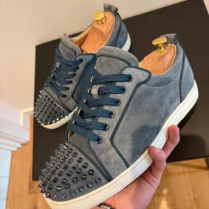 Christian Louboutin | Washed Blue. - Säljer ett par blå sneakers från Christian Louboutin i mocka med ikoniska röda sulor och coola nitar på tån. Skorna har snörning och vit platt sula, perfekt för dig som vill sticka ut med lyxig streetstyle. Grym färg och detaljer som verkligen syns. Dustbag medföljer, låda, kvitto, orderbekreftekse möts på Ostermalm eller fraktar
