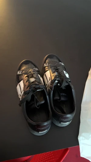 Valentino Garavani svarta sneakers - Säljer ett par svarta Valentino Garavani sneakers med vit logga på sidan  skorna är använda och lådan finns men måste ba leta fram den så utan låda 900 med låda 1200