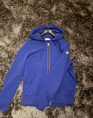 Blå hoodie från Moncler med dragkedja - Snygg blå hoodie från Moncler med luva  och snörning, samt klassisk Moncler-logga på ärmen. Tröjan har en hel dragkedja med röd, vit och blå kant, två fickor fram och ribbade muddar. Perfekt för dig som gillar stilrena och exklusiva märken. Dm för mer bilder…