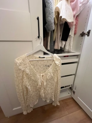 Spetsblus med volang från Gina Tricot -  spetsblus  från Gina Tricot. Blusen har långa ärmar, v-ringning med knyt framtill och volangdetaljer längs krage och ärmslut. Den är i storlek S och är använd fåtal gånger. 