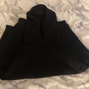 Svart hoodie med huva - Svart hoodie med stor huva och klassisk design. Tröjan har långärmade ärmar och är gjord i ett mjukt material som passar perfekt för kyliga dagar. Enkel och stilren look som funkar till många olika outfits.