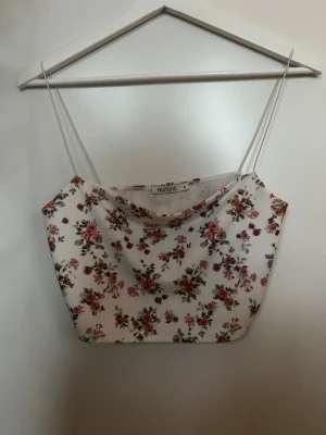 Blommig linnetopp från NLY One - Säljer en söt linnetopp från NLY One i storlek M. Toppen är vit med små blommor i rosa och rött, har tunna axelband och en mjuk, draperad halsringning. Perfekt för sommarens alla häng och passar till både jeans och kjol.