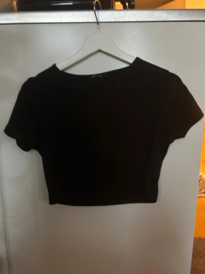 Svart croppad ribbad topp - Säljer en svart croppad topp  med ribbad struktur. Toppen har korta ärmar och en rund halsringning, perfekt för att styla med höga jeans eller kjol. Enkel och stilren design som funkar till många looks.