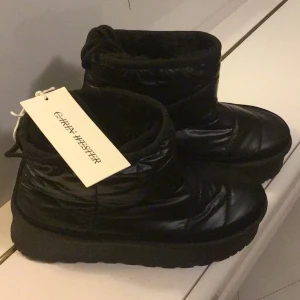 Svarta moon boots från Carin Wester - Säljer ett par nya svarta moon boots från Carin Wester med quiltad ovandel och tjock, räfflad plattformsula. Skorna är tillverkade i syntetmaterial och har en rund tå. Perfekta för vintern med sin varma och vadderade design. Strl 39 men känns som 38 ,fel storlek för mig.