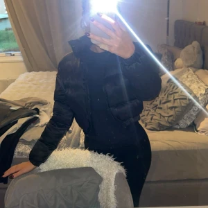 Svart croppad pufferjacka - Säljer en svart croppad pufferjacka med hög krage och dragkedja framtill. Helt ny passar även er som har storlek s