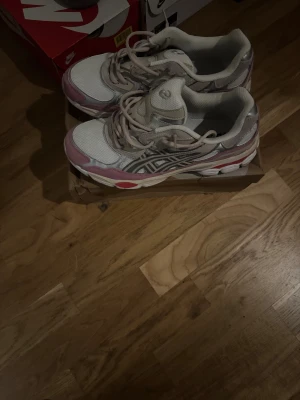 ASICS GEL-NYC sneakers beige/rosa - Säljer ett par ASICS GEL-NYC sneakers i färgen cream/real beige med rosa och röda detaljer. Skorna har mesh och mocka på ovandelen, snörning och en chunky sula med platt profil. Perfekt för dig som gillar retrovibbar och sportig stil.