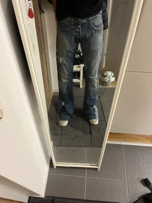 Custommade jeans från replay. - Säljer ett par blå bootcut jeans från Replay med slitna detaljer och fransade benslut. Jeansen har klassisk femficksdesign, låg midja och dragkedja. Materialet är robust denim och passformen är loose med breda ben. Perfekt för dig som gillar en avslappnad stil. Jeansen är custommade. Jag på bilden är 191 cm. Måtten är 32/36