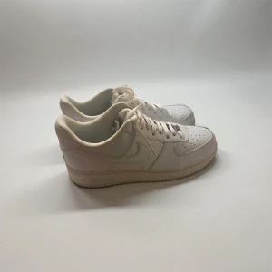 Nike Air Force 1  vita sneakers - Nike Air Force 1 sneakers i helvitt med klassisk låg siluett. Skorna har perforerad tå, snörning och en platt sula. Tillverkade i skinn med mjukt foder och ikonisk Swoosh på sidan. Perfekt för dig som gillar clean och tidlös streetstil.