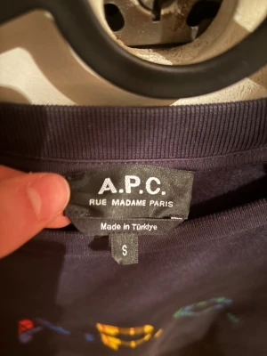 Mörkblå sweatshirt från A.P.C. - Snygg mörkblå sweatshirt från A.P.C. med färgglatt rutigt tryck på bröstet. Tröjan har rund hals, långa ärmar och en relaxed passform. Perfekt för dig som gillar stilrena plagg med en twist. Materialet är mjuk bomull som känns skönt mot huden. Nypris :2000, pris kan diskuteras vid snabb affär 