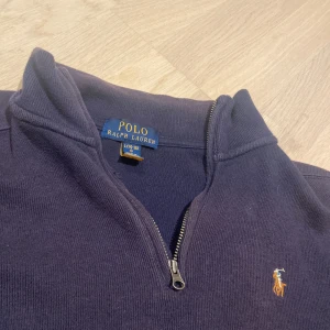 Mörkblå stickad QuarterZip från Ralph Lauren - Mörkblå stickad tröja från Polo Ralph Lauren med klassisk broderad logga på bröstet. Tröjan har lång ärm, half zip och en mjuk, skön känsla. Perfekt för dig som gillar stilrena och tidlösa plagg med snygga detaljer.