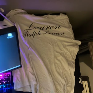 Vit t-shirt från Ralph Lauren - Säljer en vit t-shirt från Ralph Lauren med stor svart logotyp på bröstet. Klassisk rund hals och korta ärmar, perfekt för en clean och stilren look. Mjuk bomull som känns skön mot huden.