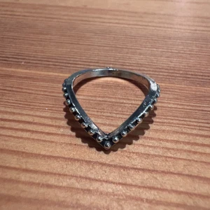 Silvrig V-formad ring med pärlor - Snygg ring i silverfärgad metall med en unik V-formad design. Ringen är dekorerad med små pärlor längs hela kanten som ger extra glans och cool detalj. Perfekt för dig som gillar att sticka ut med dina accessoarer.