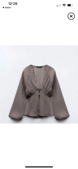 Plisserad grå blus från Zara - Superfin plisserad blus i grått från Zara med v-ringning och knyt framtill. Långa vida ärmar och lätt transparent material ger en luftig känsla.