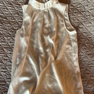 Vit sidenblus från Stockh lm - Supersnygg vit blus i siden från Stockh lm, med hög krage och veckade detaljer framtill. Blusen är ärmlös och har en diskret dragkedja i nacken. Perfekt för dig som gillar stilrena och eleganta plagg med lyxig känsla.