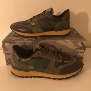 Valentino Garavani Rockrunner sneakers - Snygga Valentino Garavani Rockrunner sneakers i camouflage-mönster med gröna, bruna och beige toner. Skorna har detaljer i mocka och skinn, klassisk snörning och platt sula med nitar vid hälen. Perfekta för dig som vill sticka ut med exklusiva och trendiga sneakers.