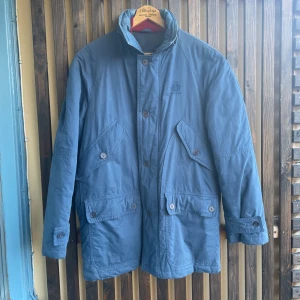 blå vinterjacka Paul & Shark - Tjock mörkblå vinterjacka från det välkända och väldigt exklusiva italienska företaget Paul & Shark som har fokus på seglarkläder. Jackor i samma genre som denna modell finns idag att köpa till nypris upp emot 30.000kr.   Modellen är äldre och finns ej att hitta i något av deras sortiment idag. Trots åldern är jackan i väldigt bra skick. Lite solblekning skulle jag gissa på men i mina ögon tillför det bara utseendemässigt.   Jackan är fodrad och varm och har många fickor. Passar till M/L.