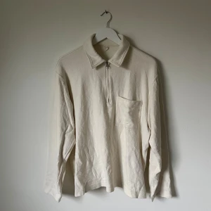 Beige half zip tröja från ARKET - Säljer en beige långärmad tröja från ARKET i storlek M. Tröjan har en klassisk krage, half zip-dragkedja framtill och en bröstficka. Materialet är mjuk bomull som känns skönt mot huden. Perfekt för dig som gillar stilrena och enkla plagg. 5I7