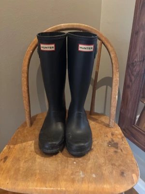 Hunter stövlar - Klassiska svarta Hunter stövlar i gummi med rund tå och platt sula. Höga skaft och tydlig Hunter-logga framtill. Perfekta för regniga dagar och leriga äventyr. Kan vara i barnmodell är lite osäker men tror inte det spelar någon roll🩷