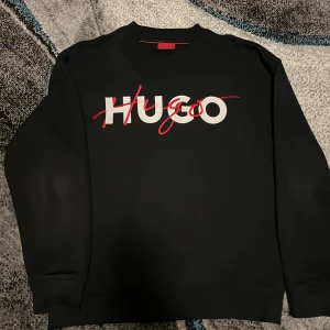  Hugo Boss  - Svart sweatshirt från Hugo med stort vitt och rött logotryck över bröstet. 