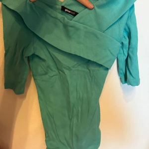 Turkos ribbad omlottop från Gina Tricot - Säljer en turkos ribbad omlottop från Gina Tricot. Toppen har lång ärm och omlottdesign som ger en snygg och trendig look. Perfekt att styla med jeans eller kjol för en fräsch vardagsoutfit.