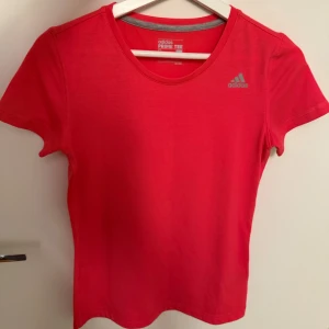 Ny Adidas korall t-shirt, storlek S - •Aldrig använd snygg korall t-shirt från Adidas med klassisk rund halsringning och diskret logga på bröstet. Lappen är inte kvar. •Perfekt för träning eller chill dagar.  •Tillverkad i ett mjukt och lätt material som andas.  Djur och rökfritt hem. 